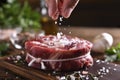 Hand sprinkling salt on fresh raw beef meat on a cutting board