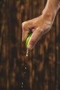 Hand squeeze lime with lime drop on wooden background Royalty Free Stock Photo