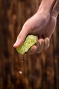 Hand squeeze lime with lime drop on dark wooden background