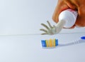The hand squeezes the toothpaste from the tube onto the toothbrush.