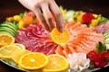 hand squeezing lemon on a colorful sashimi platter