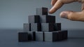 A hand stacking black blocks into a pyramid structure.