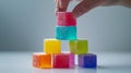 Hand stacking colorful cubes in a pyramid shape.