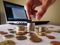 Hand Stacking up coins and a laptop computer