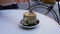 Hand stirring coffee in ceramic cup outdoors on cafe table beside bicycle in urban setting with spoon creating rich frothy texture Royalty Free Stock Photo