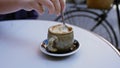Hand stirring coffee in ceramic cup outdoors on cafe table beside bicycle in urban setting with spoon creating rich frothy texture Royalty Free Stock Photo