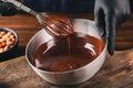 Hand stirring with a whisk melted dark chocolate in a metal bowl on a wooden table.