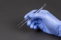 Hand of surgeon in blue medical glove holding a tweezers  on dark background Royalty Free Stock Photo