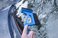 Hand sweeping snow from the car windshield with an ice scraper and broom, important winter tool for safe driving in the cold Royalty Free Stock Photo