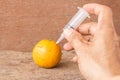 Hand with syringe and tangerine on wooden