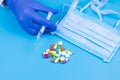 Hand with syringe, various pills and medical mask on a blue background. Medicine. Treatment