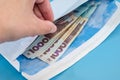 Hand takes out 1000 hryvnia in a white envelope. Blue background. Close-up.