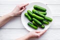 Hand takes plate with fresh cucumbers. Grey wooden background top view