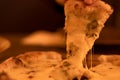 A hand takes a slice of hot four cheese pizza with stretched cheese close-up in warm evening light. Man takes first slice Royalty Free Stock Photo