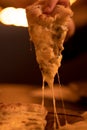 A hand takes a slice of hot vegetarian four cheese pizza with stretched cheese close-up in warm evening light.