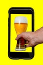 Hand is taking beer from phone on yellow background