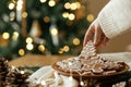 Hand taking christmas gingerbread cookie with icing from plate on festive table with decorations against golden tree lights. Merry Royalty Free Stock Photo