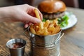 hand taking a fry from a stylish metallic serving pail, burger in back