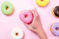 Hand taking pink donut on pastel background