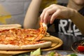 Hand, taking slice of pepperoni pizza from round wooden tray Royalty Free Stock Photo