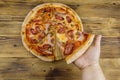 Hand taking slice of tasty pizza. Hot italian pizza on wooden table. Top view Royalty Free Stock Photo