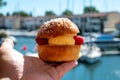 Hand with Tarte tropezienne or La Tarte de Saint-Tropez - dessert pastry consisting of filled brioche with cream and fresh berries