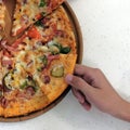 The hand of a teenager takes a piece of pizza from a wooden plate. White table background. A square picture. Royalty Free Stock Photo