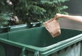 Hand throwing crumpled paper bag in trash on street over tree