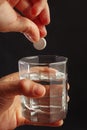 Hand throwing an effervescent pill from headache in glass of water on a dark background. Royalty Free Stock Photo