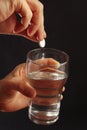 Hand throwing an effervescent tablet in a glass of water on dark background. Royalty Free Stock Photo