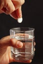 Hand throwing an effervescent tablet from headache in a glass of water on dark background. Royalty Free Stock Photo