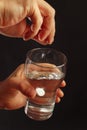 Hand throwing a soluble pill in a glass of water on dark background. Royalty Free Stock Photo