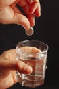 Hand throwing a soluble pill from headache in a glass of water on dark background. Royalty Free Stock Photo