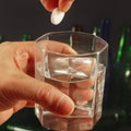 Hand throwing a soluble tablet from hangover in a glass of water on dark background. Royalty Free Stock Photo