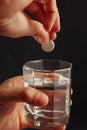 Hand throwing a soluble tablet from headache in a glass of water on dark background. Royalty Free Stock Photo