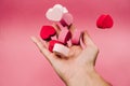 A hand throwing some little hearts of sponge with different colors on a pink background. The hearts are dispersed on the hand. San