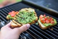 hand toasting bread slice on a grill for avocado bruschetta