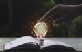 Hand toching light bulbs and book opening on wooden table.