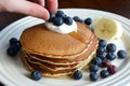 hand topping pancake stack with blueberries, yogurt on side Royalty Free Stock Photo