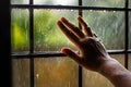 hand touching window bars with raindrops