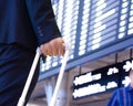 Hand of traveling businessman with baggage in front of airport timetable