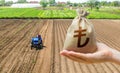 Hand with a Turkish lira money bag on the background of a farm field with a tractor. Subsidies support for agricultural producers