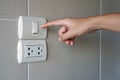 Hand turn on a power, Finger pushing light switch button with plug on ceramic tile wall in bathroom. Royalty Free Stock Photo