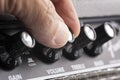 Hand turning up the volume of a guitar amplifier, treble and bass control knobs out of focus , equalization dials close up