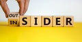 Hand turns a cube and changes the expression `insider` to `outsider` or vice versa. Beautiful yellow table, white background. Royalty Free Stock Photo