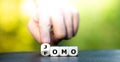 Hand turns dice and changes the abbreviation FOMO fear of missing out to JOMO joy of missing out