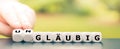 Hand turns dice and changes the German word `glÃÂ¤ubig` religious to `unglÃÂ¤ubig` irreligious.