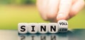 Hand turns a dice and changes the German word `sinnlos` `meaningless` in English to `sinnlvoll` `meaningful` in English