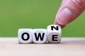 Hand turns a dice and changes the word `owe` to `own`. Royalty Free Stock Photo