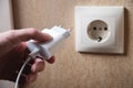 Hand turns on, turns off charger in electrical outlet on wall. White charger for phone in womans hand close-up Royalty Free Stock Photo